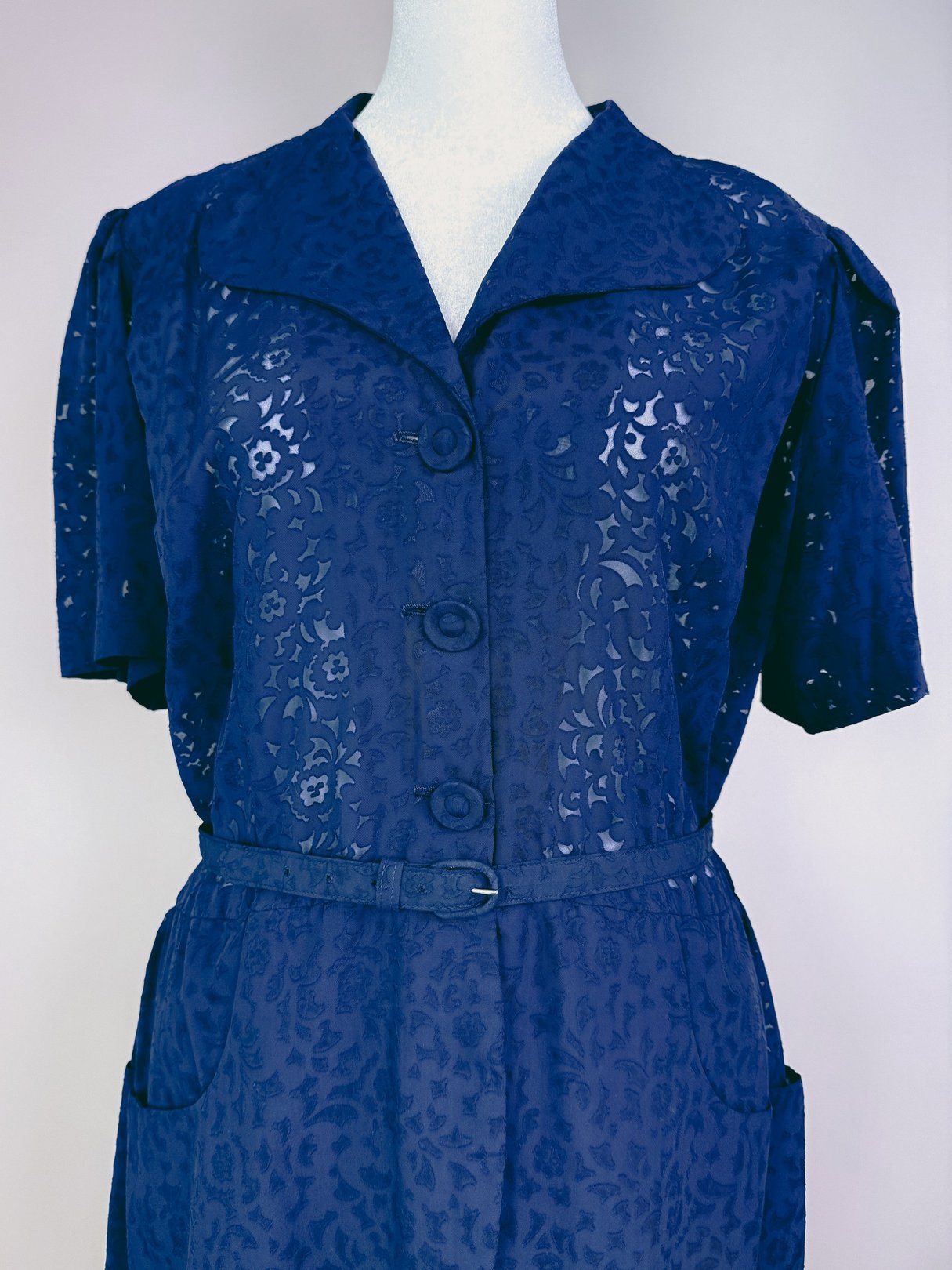 Navy blue 1940s women's dress featuring a button-up front, short sleeves, a collar, and a belted waist with pockets.