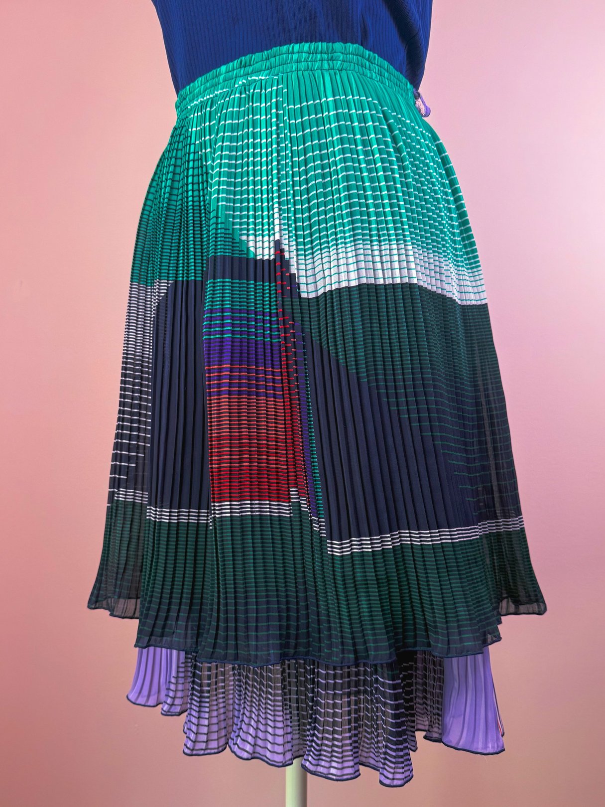 Green pleated skirt featuring a multicolored abstract pattern, inspired by 1970s fashion.
