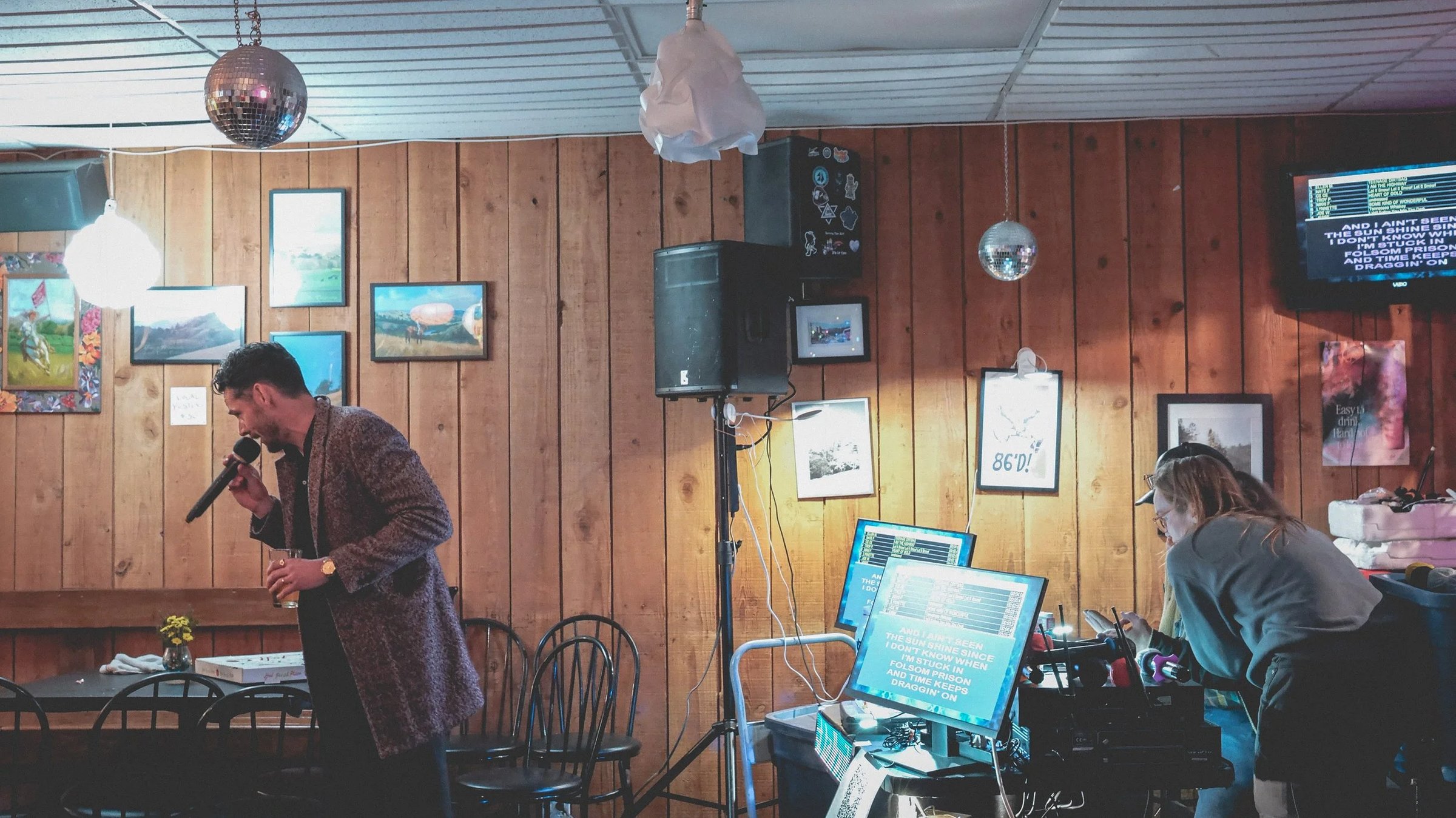 A speaker on a stand next to a computer monitor displaying text, in a room with wooden paneling and framed photos.