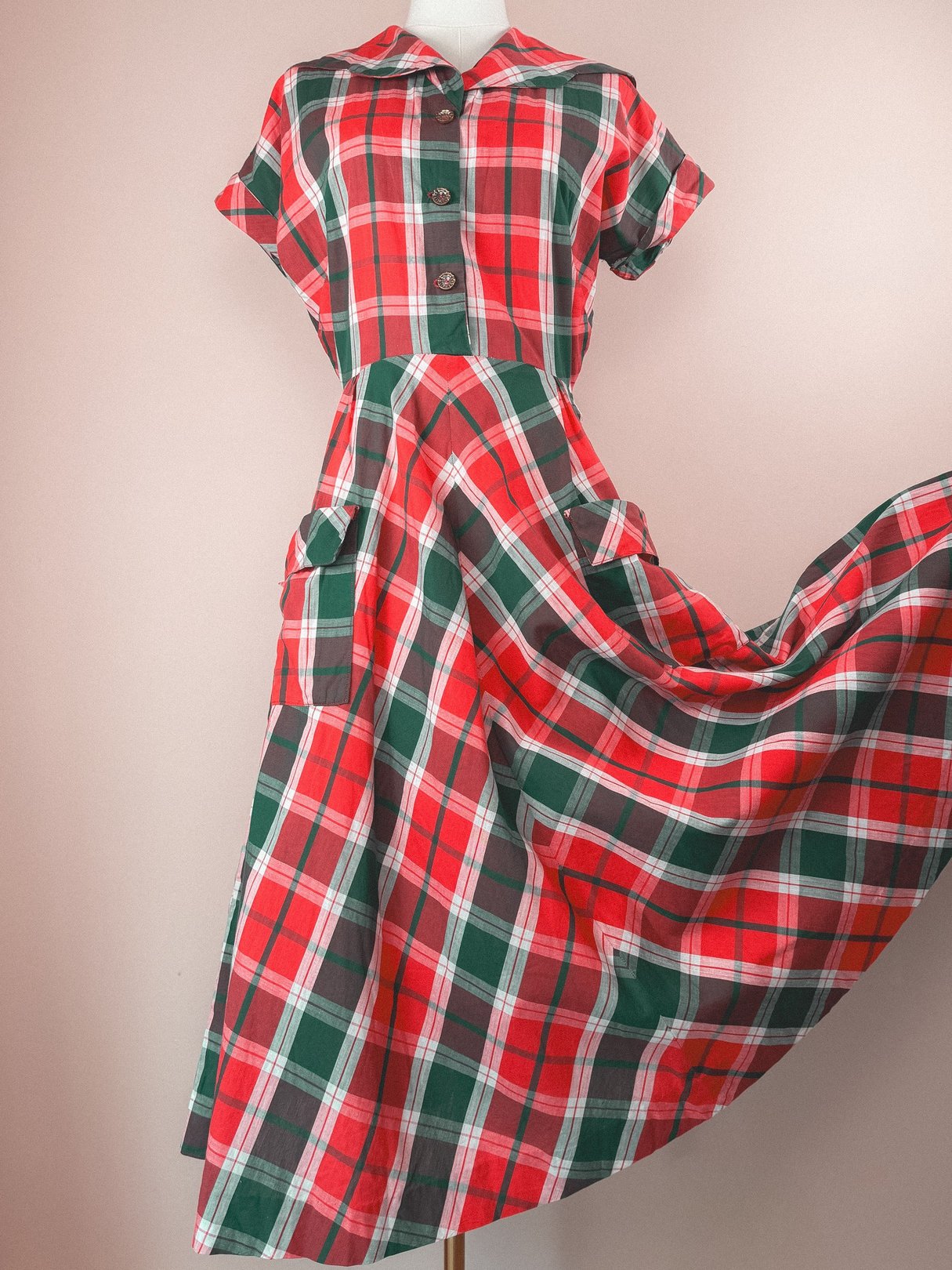 Red and green plaid dress with short sleeves, a collar, front buttons, and a flared skirt, reflecting a 1950s style for women.