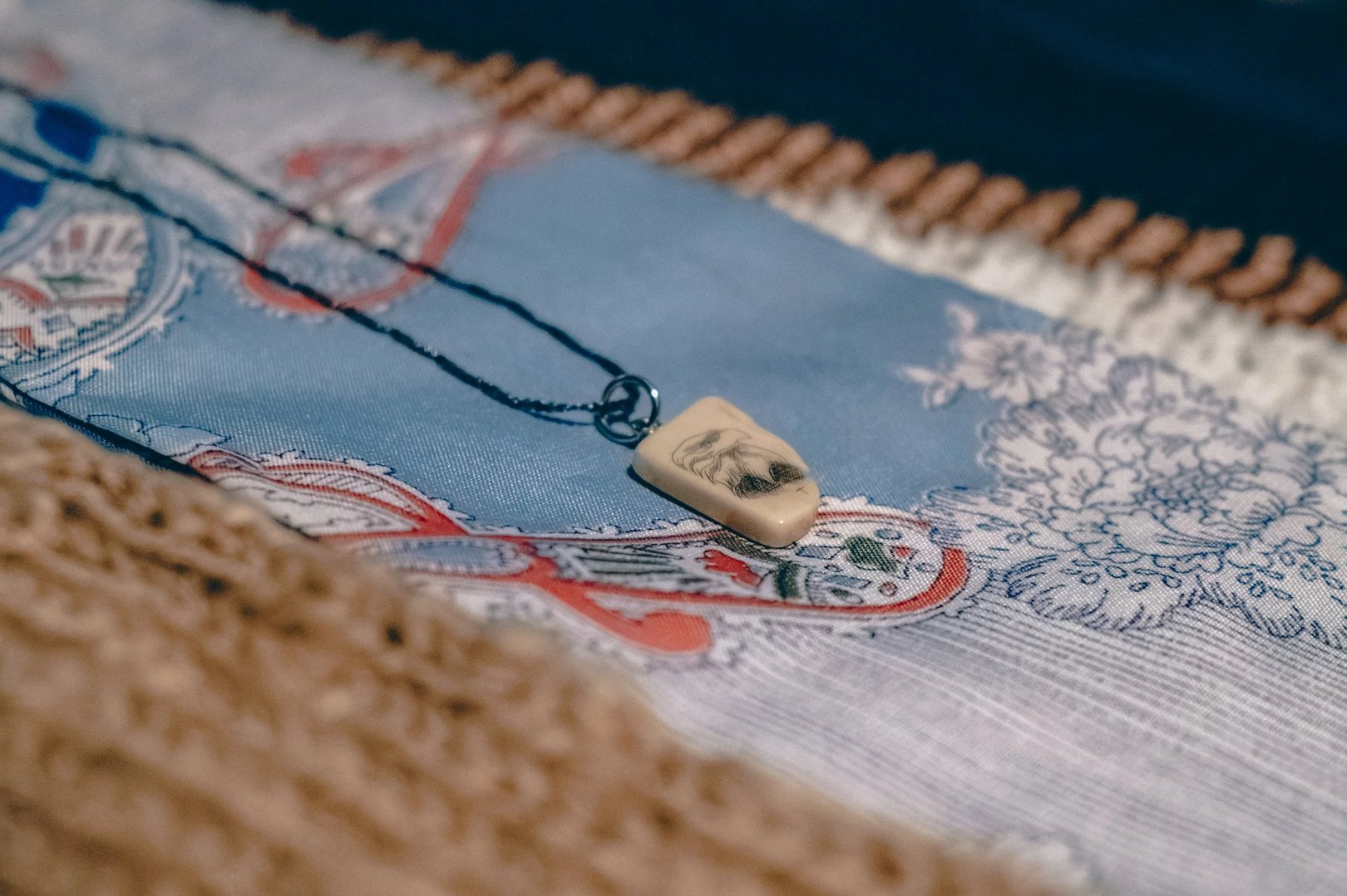 A carved pendant featuring an intricate design resting on a patterned fabric background.