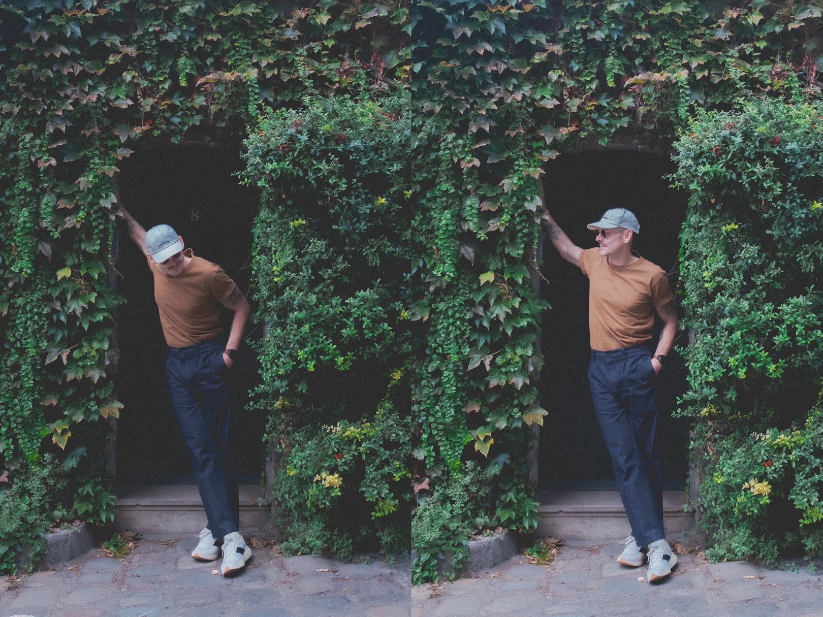 Two individuals stand on either side of a doorway partially covered in green foliage and ivy, showcasing a natural, lush outdoor environment.