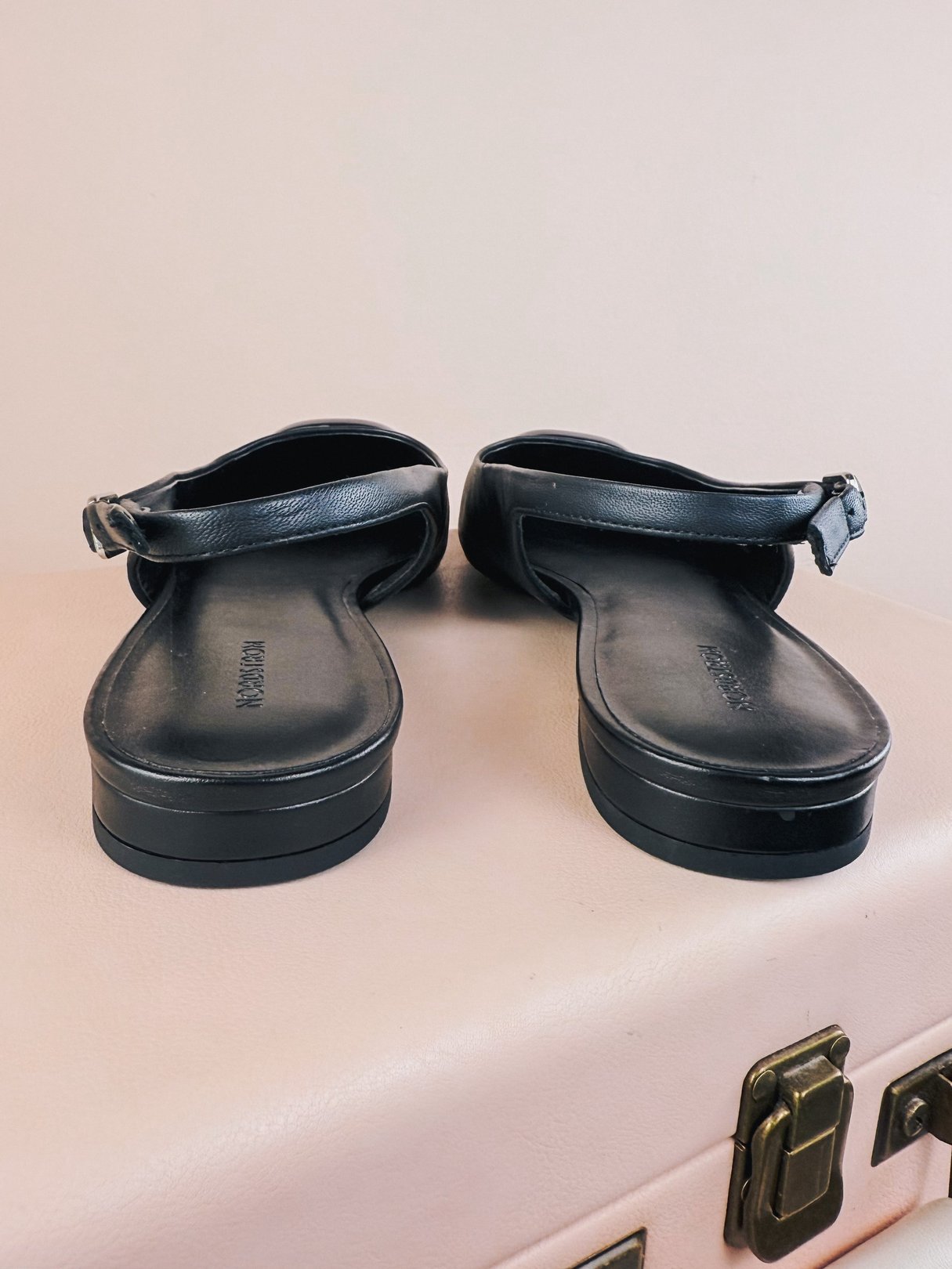 Black women's slingback flat shoes with a simple design, showcasing a back view and a flat sole, reflective of 1960s fashion.