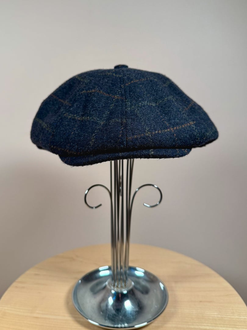 Navy blue tweed cap with a rounded shape and subtle pattern, displayed on a stand.
