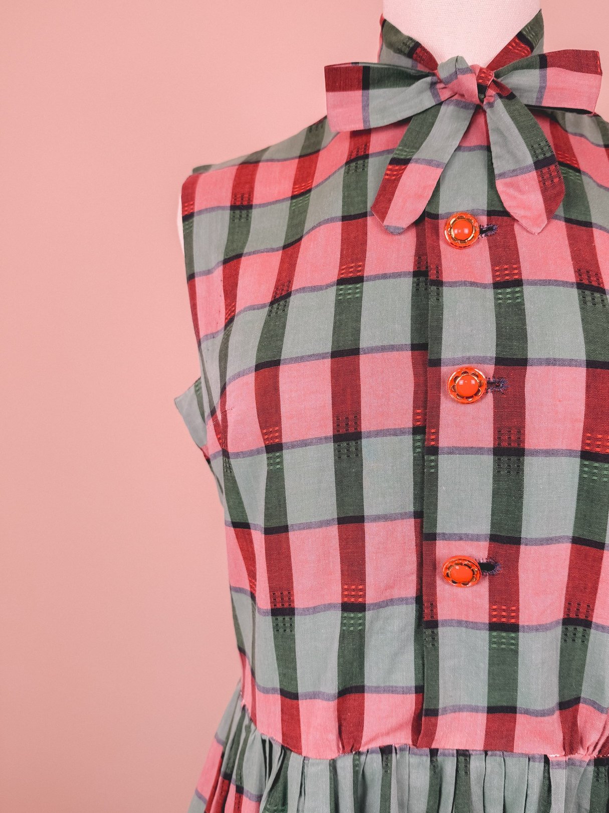 Red and green plaid dress featuring a sleeveless design and front button details, inspired by 1950s fashion.