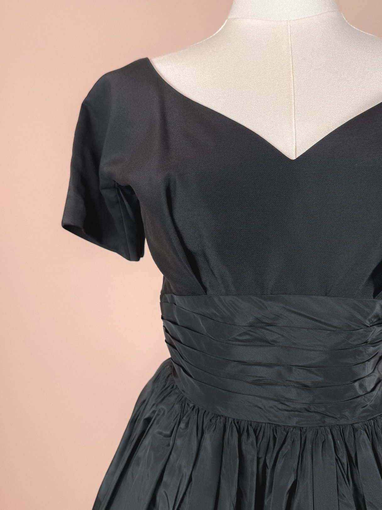 Black 1950s-style dress featuring a fitted bodice with short sleeves and a pleated waist.