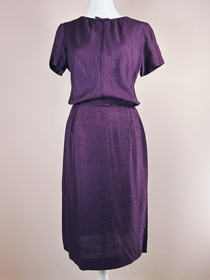 A purple 1960s women's dress with short sleeves and a fitted waist, featuring a subtle textured fabric.