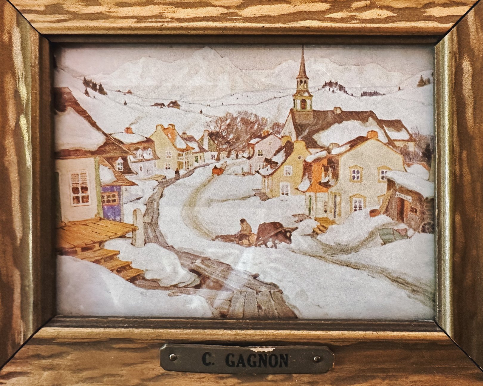 Framed artwork titled "Village in the Laurentian Mountains" by C. Gagnon, depicting a snow-covered village scene with houses, a church steeple, and a horse-drawn carriage, featurin