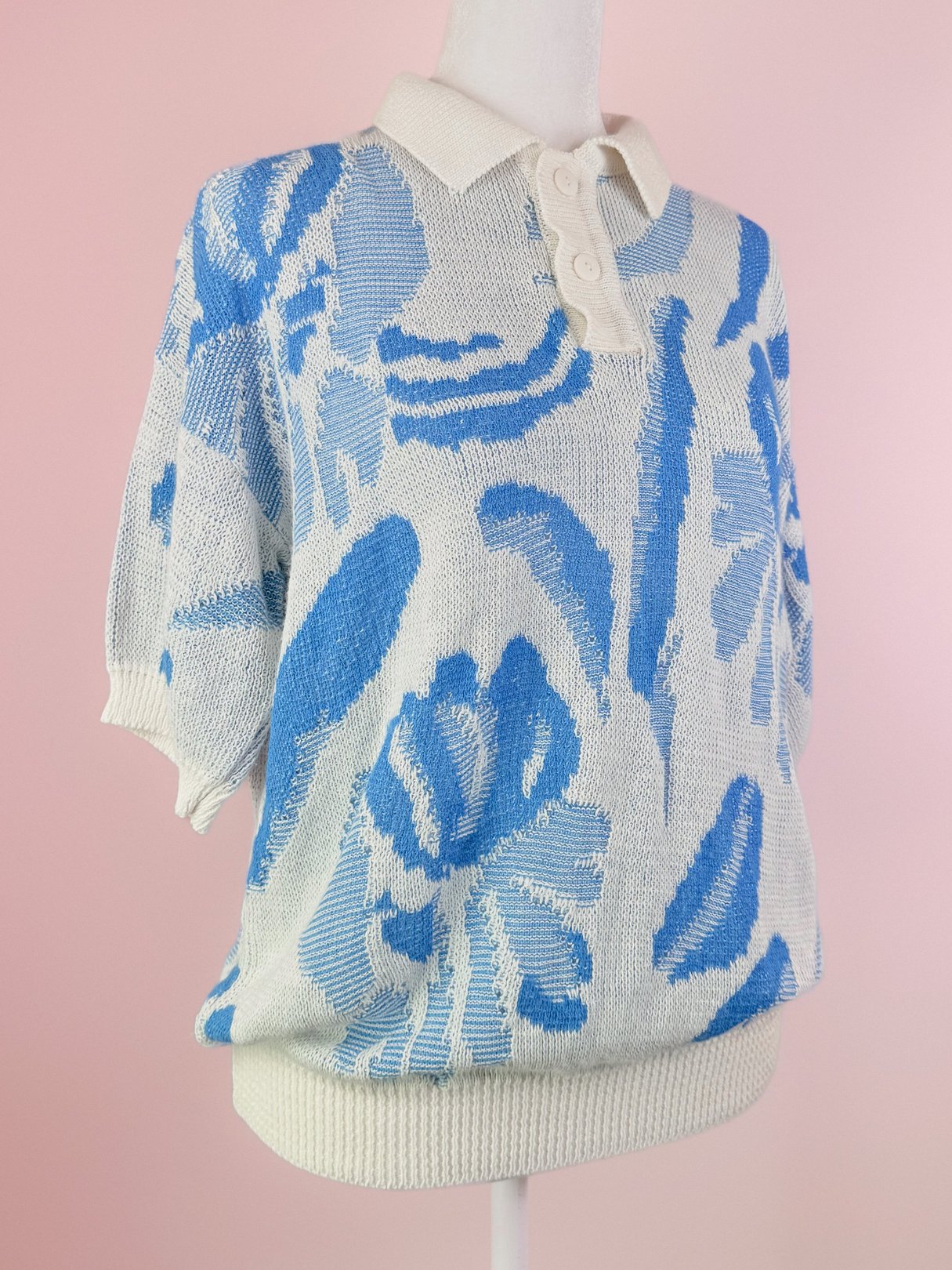Short-sleeved white knit polo sweater with blue floral patterns, featuring a collared neckline and button placket.