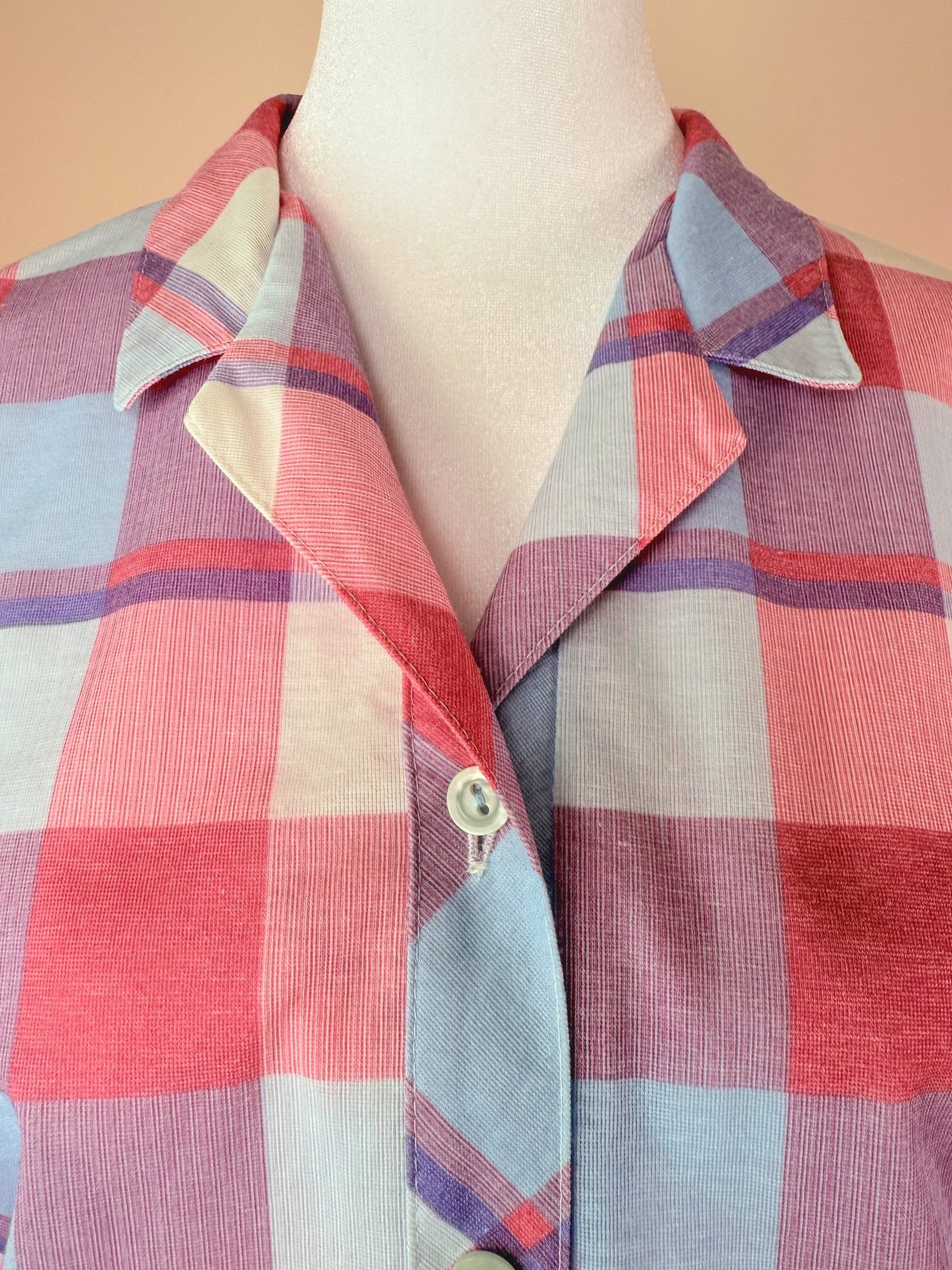 A close-up of a button-down dress featuring a purple, pink, and light blue plaid pattern with a collared neckline.