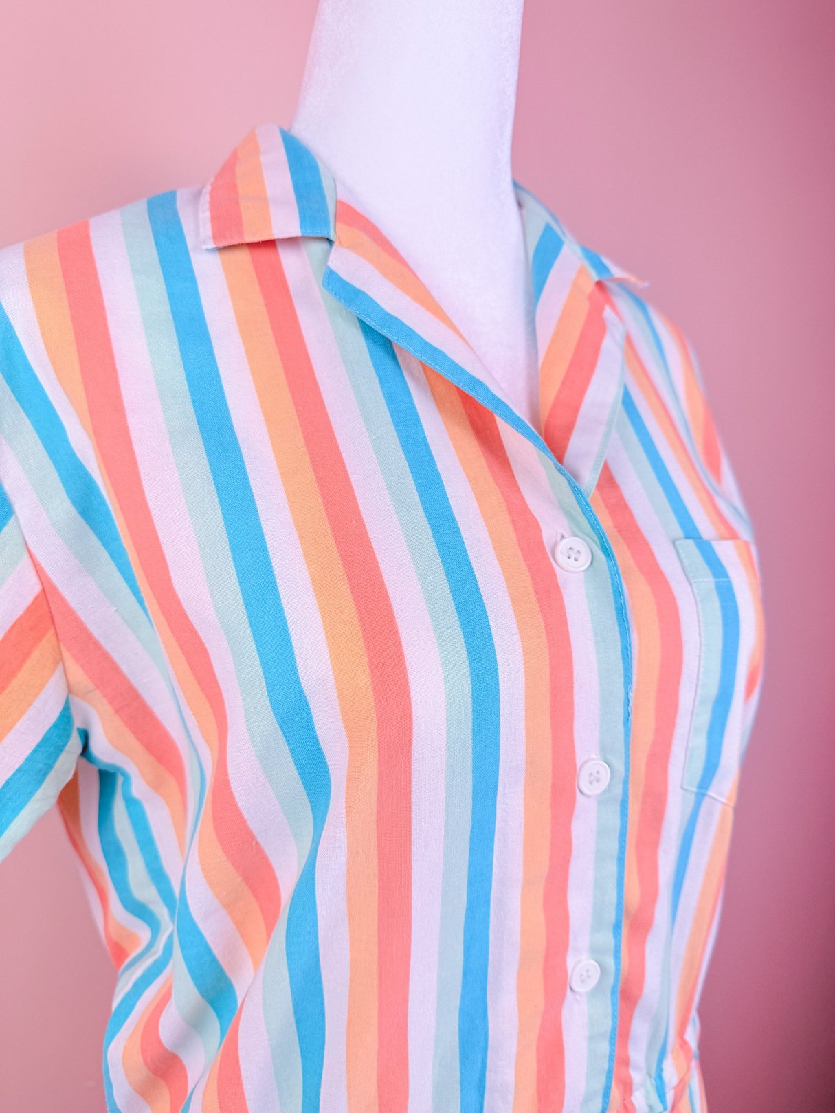 Colorful striped romper in blue, orange, and pastel shades, featuring a collar and buttons, reflecting 1980s women's fashion.