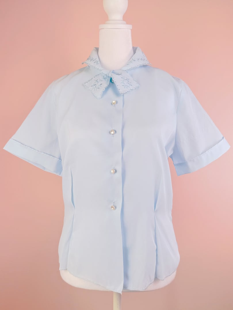 Powder blue blouse for women featuring a collar with embroidered detail and pearl buttons, styled in a 1950s design.