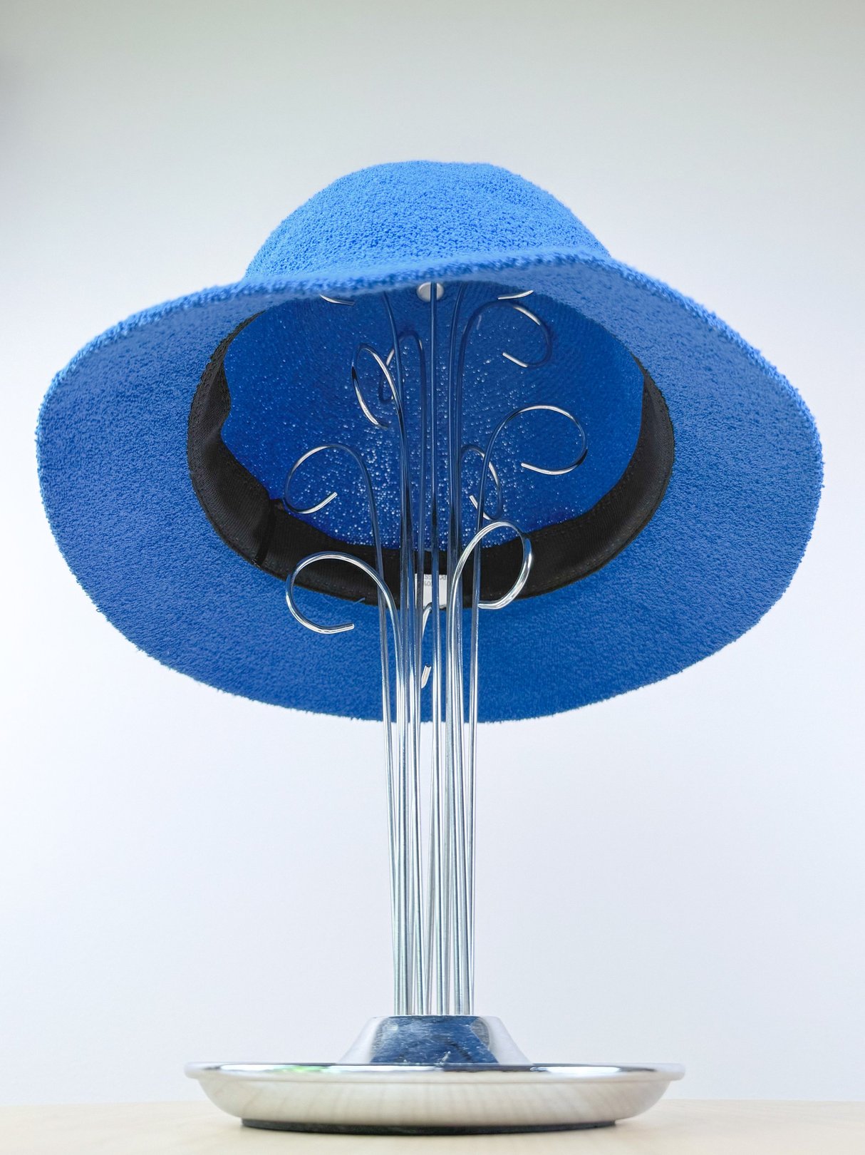 Electric blue bucket hat displayed on a silver stand.