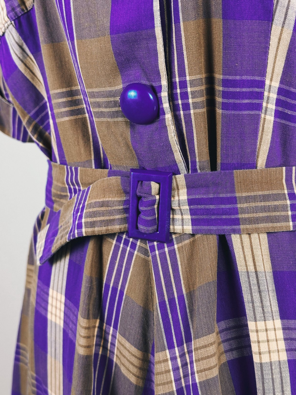 Purple plaid dress featuring short sleeves, a wide belt with a matching buckle, and a vintage 1950s style.