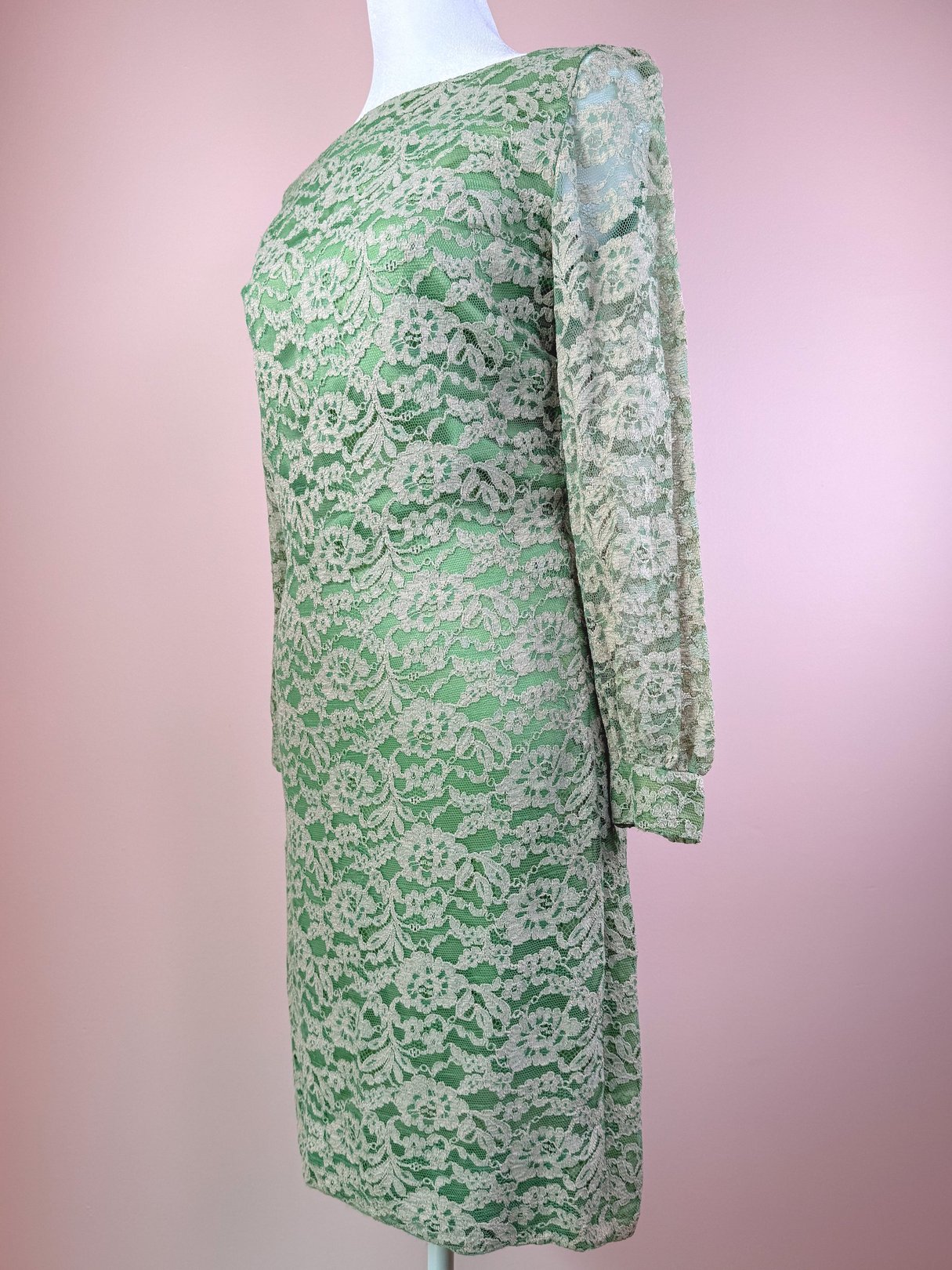A seafoam green 1960s women's dress featuring a lace overlay and long sleeves, displayed on a mannequin against a pink background.