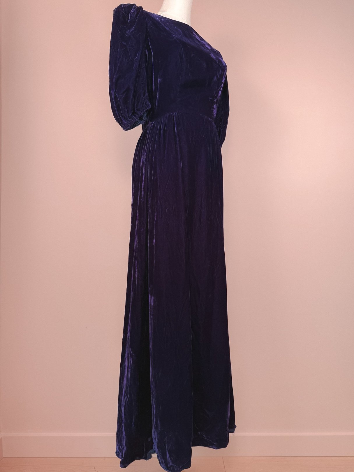 A floor-length purple velvet dress with a flowing silhouette, styled for women, reflecting 1960s fashion.