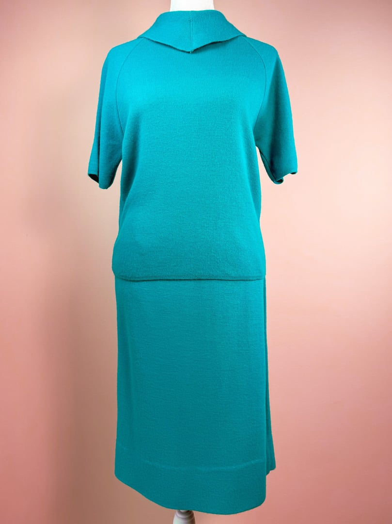 Teal green 1960s knit skirt set featuring a short-sleeve top and a knee-length skirt, displayed against a pink background.