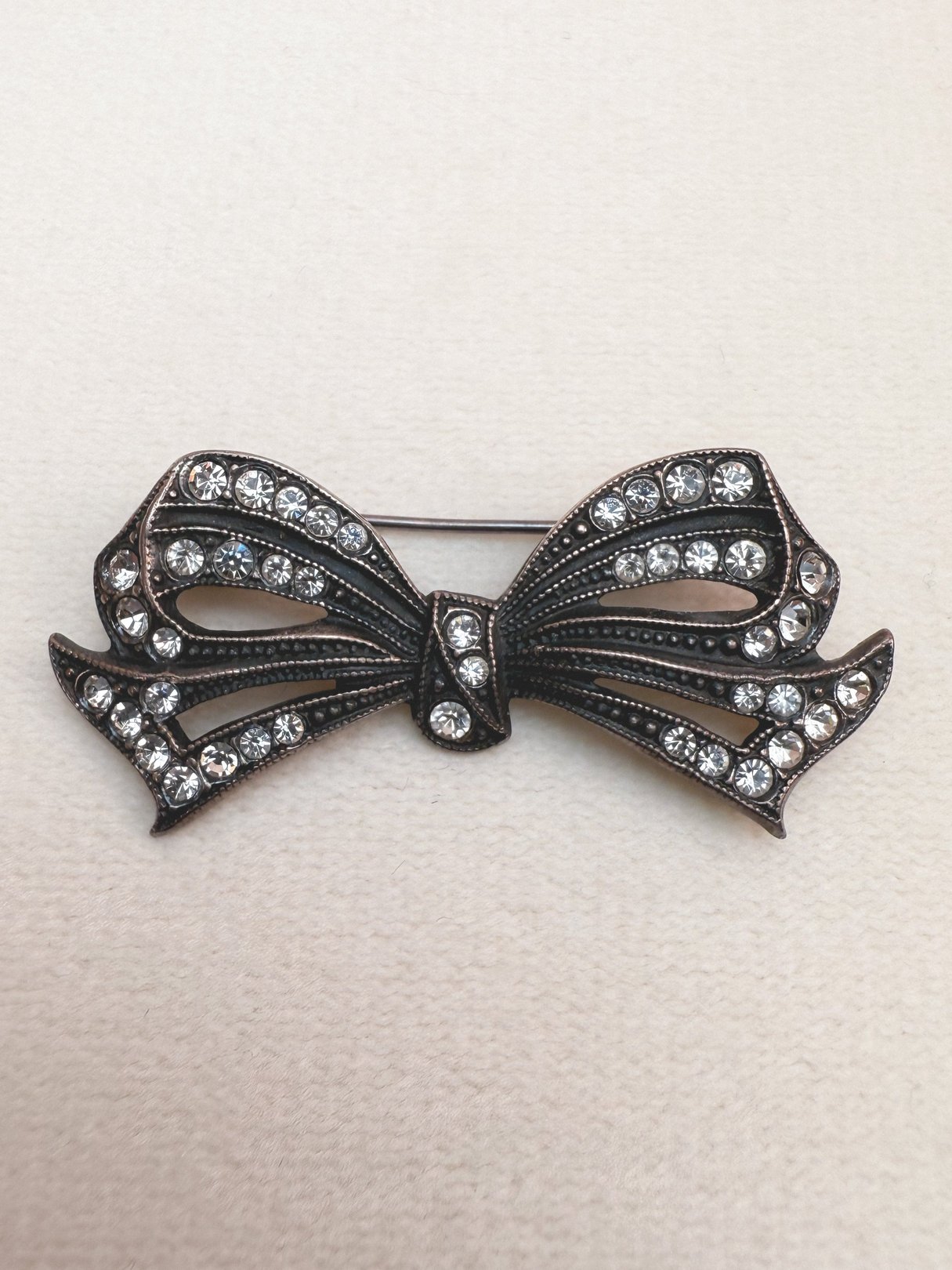Silver 1970s deco bow pin embellished with rhinestones, designed as a women's jewelry accessory.