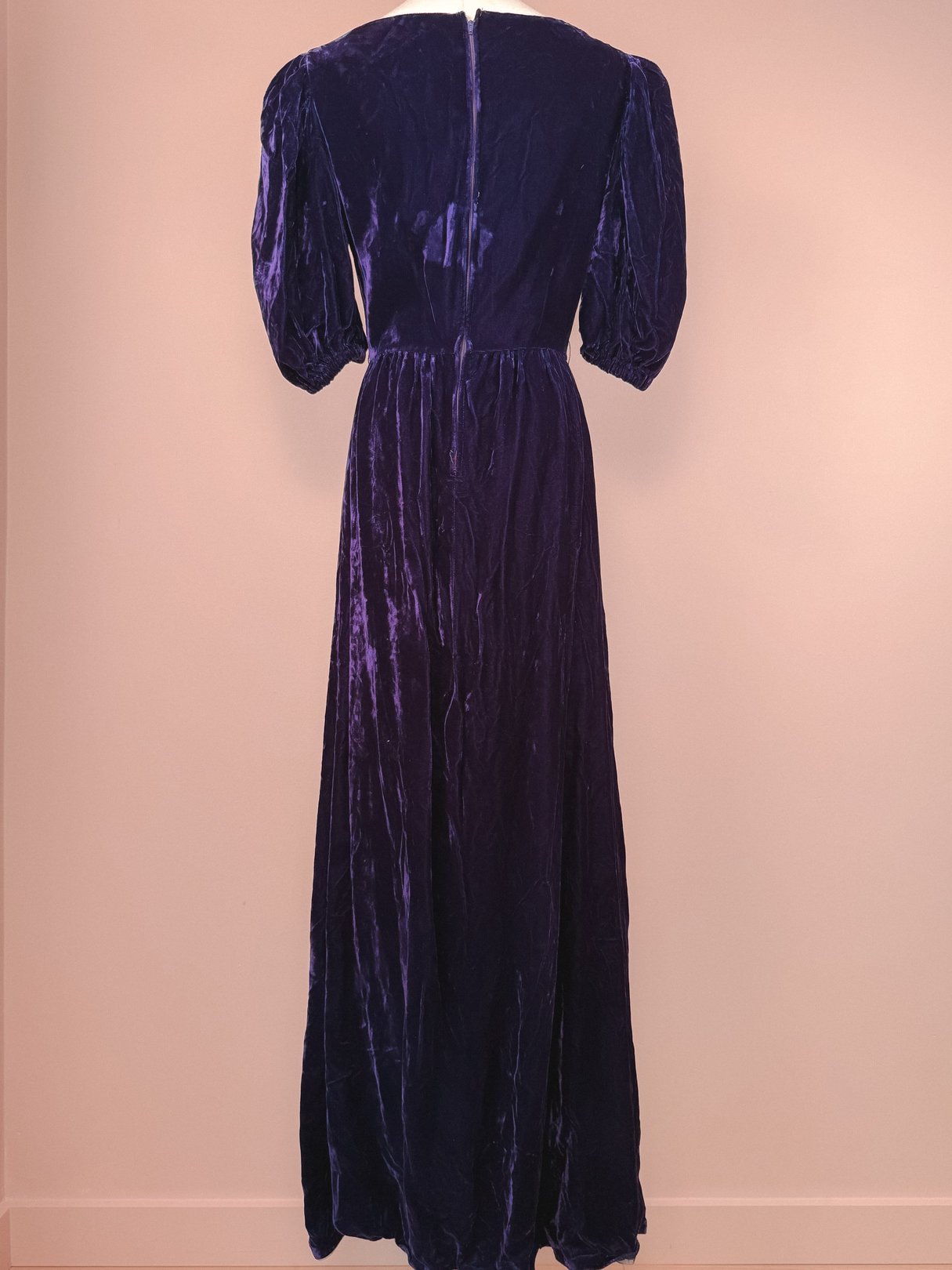 Back view of a long purple velvet dress with puffed sleeves and a zipper closure, styled in a 1960s design for women.