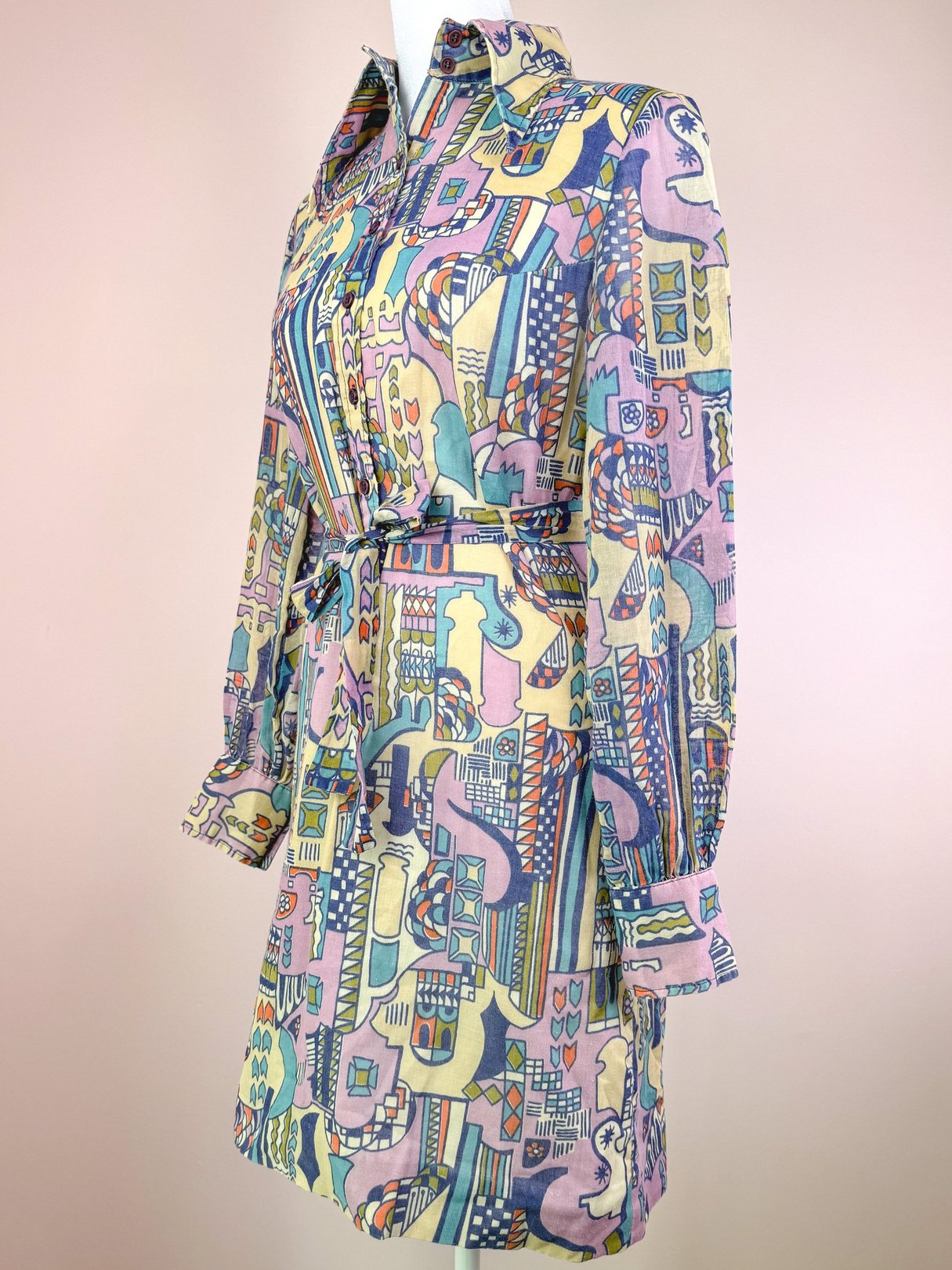 Cream-colored 1970s Metropolis dress featuring a colorful abstract pattern, long sleeves, and a belted waist.