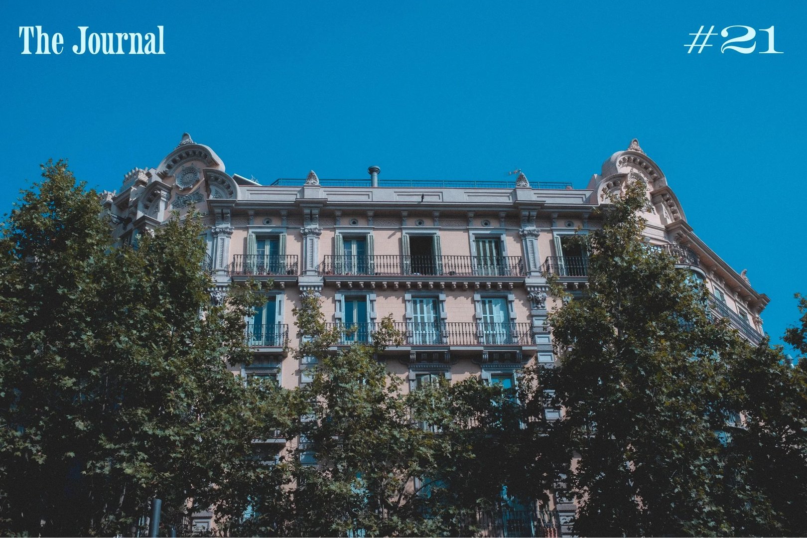 A historic building with ornate architecture under a clear blue sky, framed by trees.