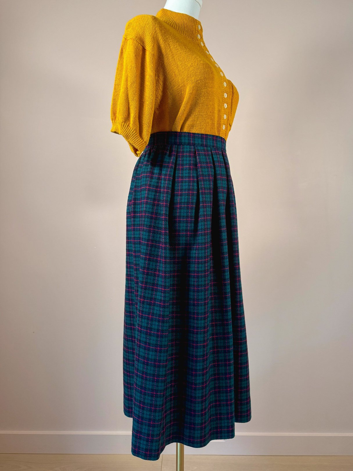 A green plaid skirt with a high waist and pleats, paired with a short-sleeved mustard yellow cardigan.