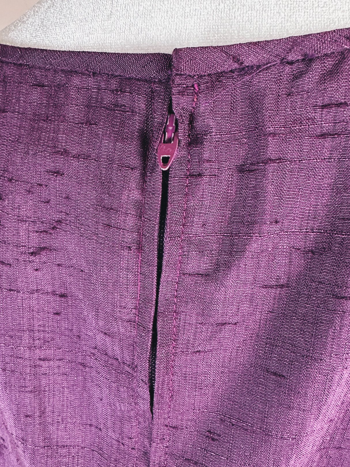 Close-up of the back zipper detail of a purple dress from the 1960s, featuring a textured fabric.
