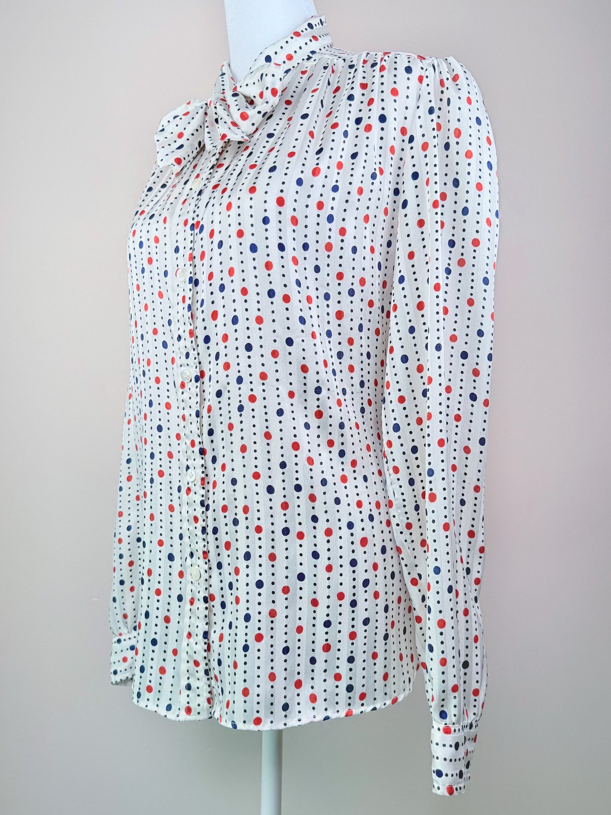1980s women's blouse featuring a white fabric with red and navy polka dots, a high neckline, and long sleeves.