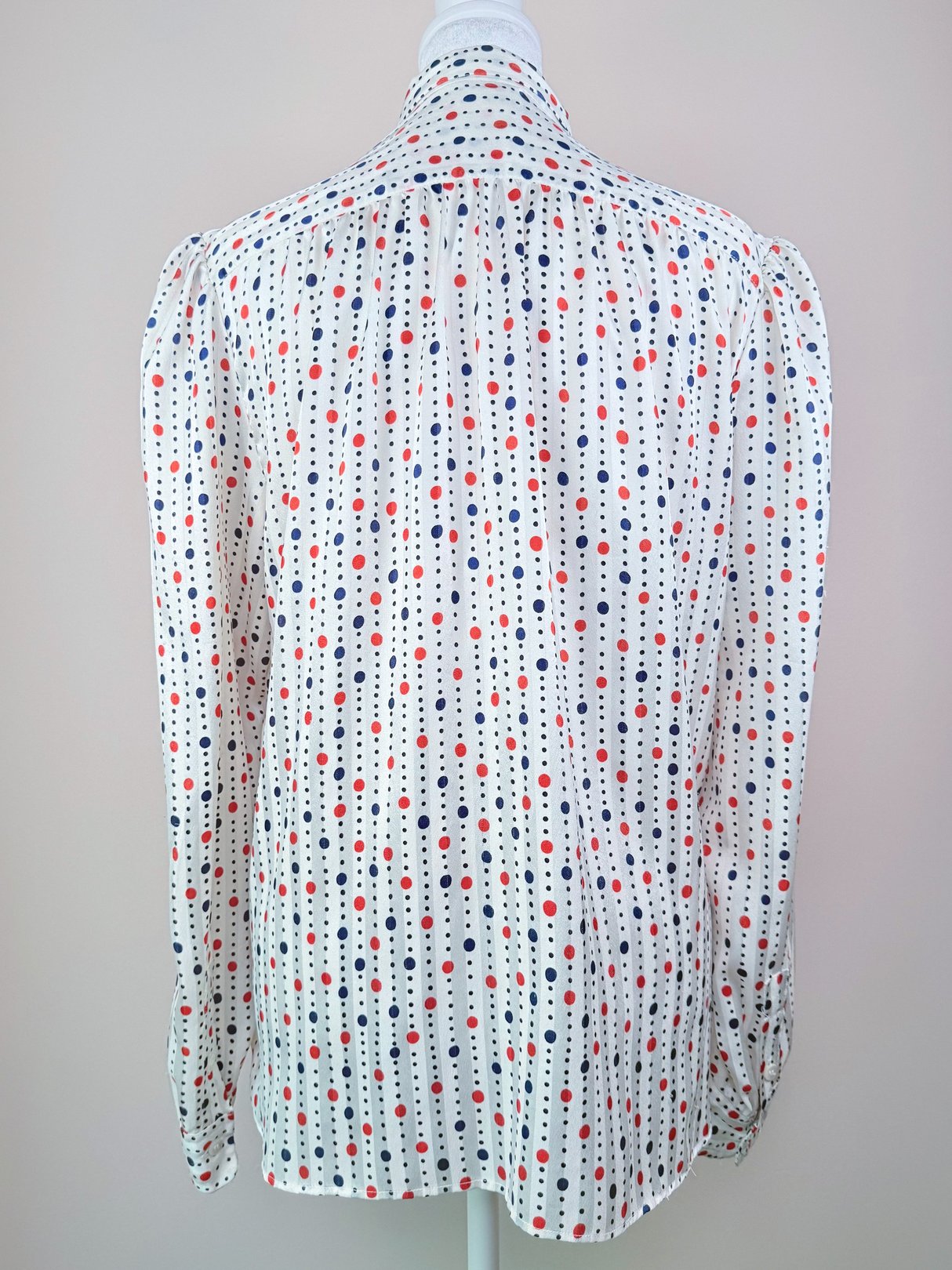 Back view of a women's 1980s blouse featuring a white fabric with red, blue, and black polka dots.