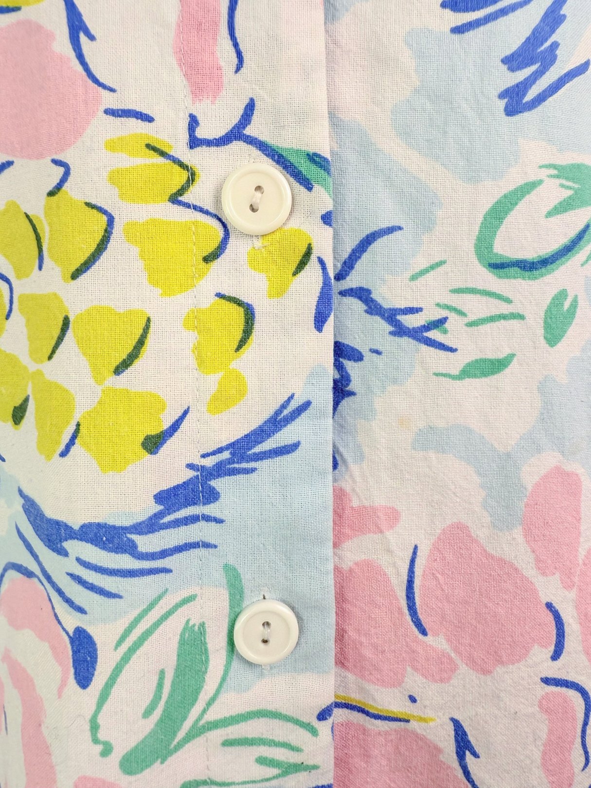 Pineapple Party Romper in blue featuring a vibrant 1980s floral print with yellow, pink, and green colors, and white buttons.