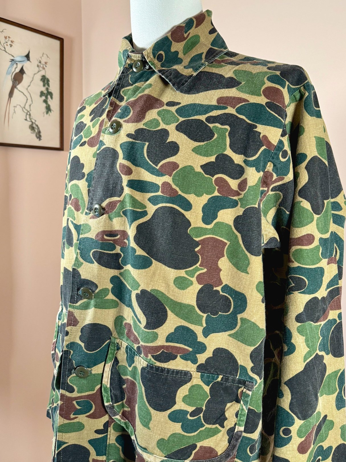 Men's 1970s camouflaged green jacket featuring a collar and front pocket.
