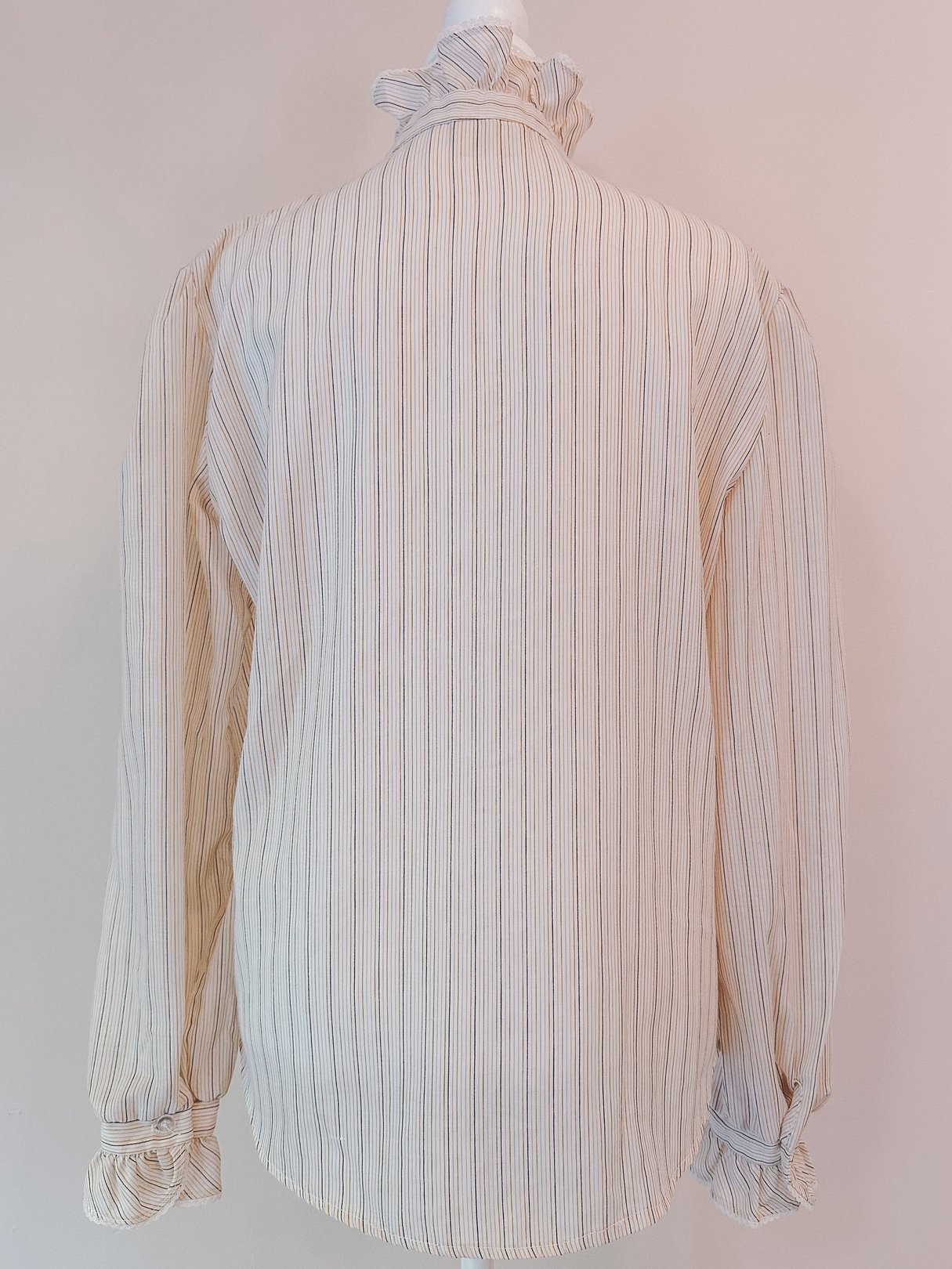 Cream blouse with a ruffled neck, featuring intricate pink, orange, and blue stripes, designed for women and reflective of 1970s fashion.
