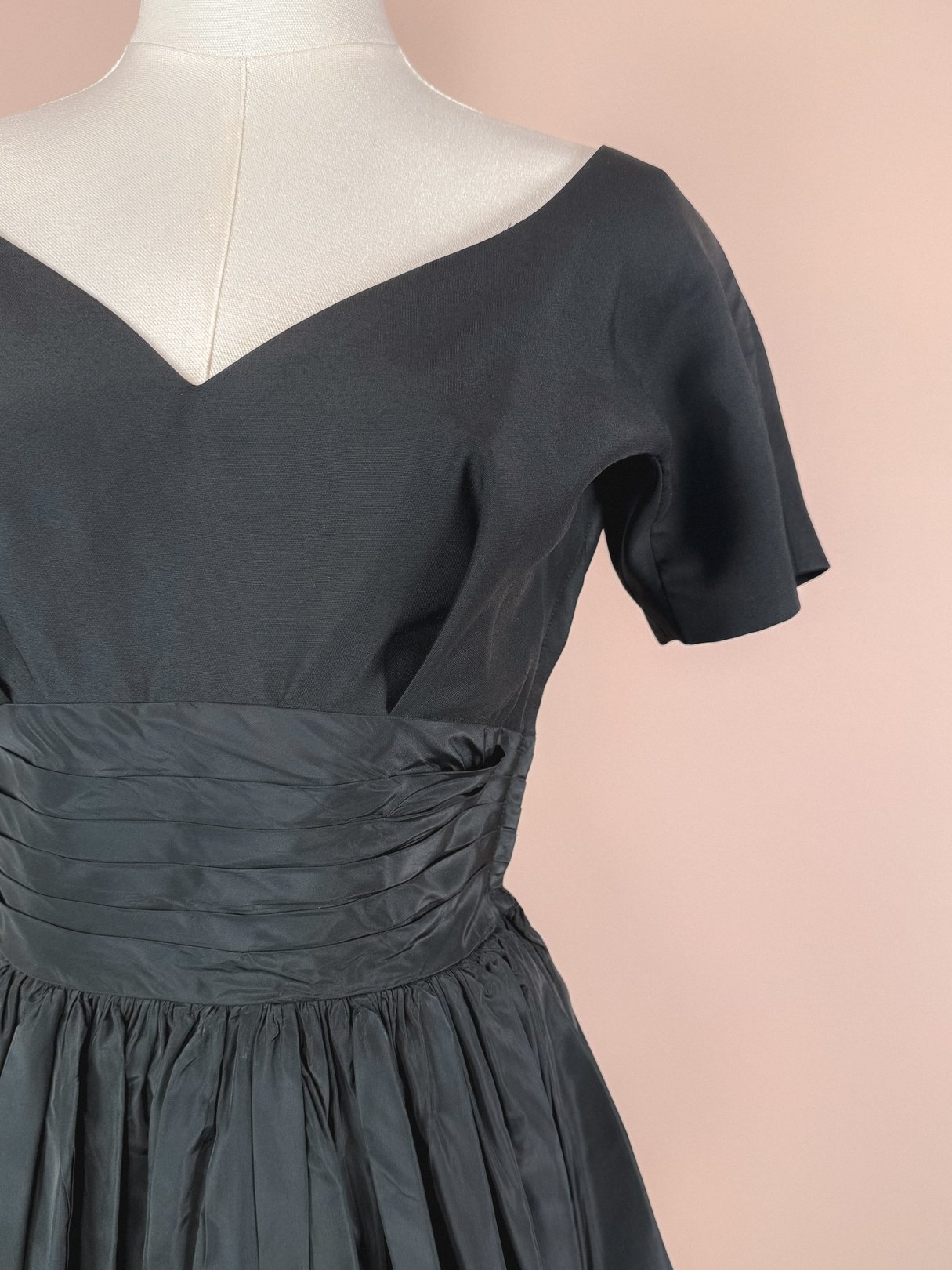 Black 1950s-style women's dress featuring a v-neckline and ruched waist detail.