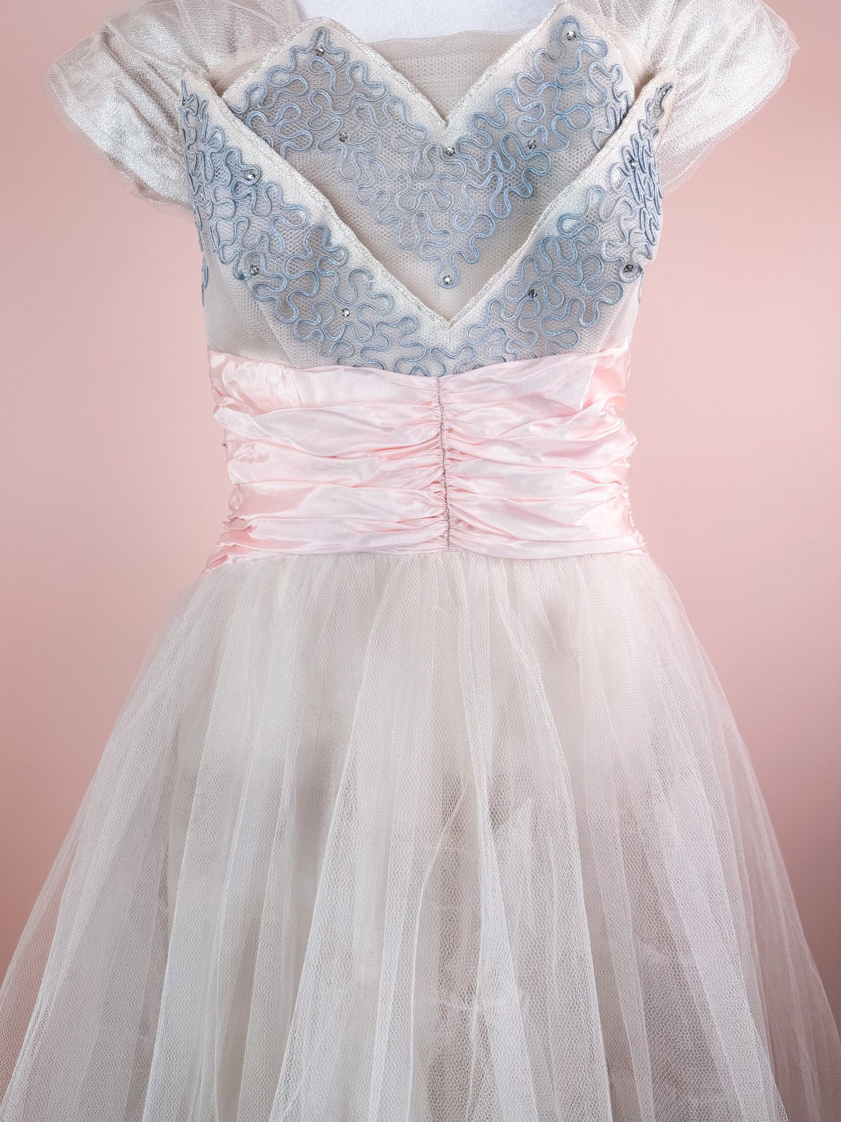 Silver 1950s women's dress featuring a sparkling bodice with intricate blue detailing and a ruched pink waistband, complemented by a flowing tulle skirt.
