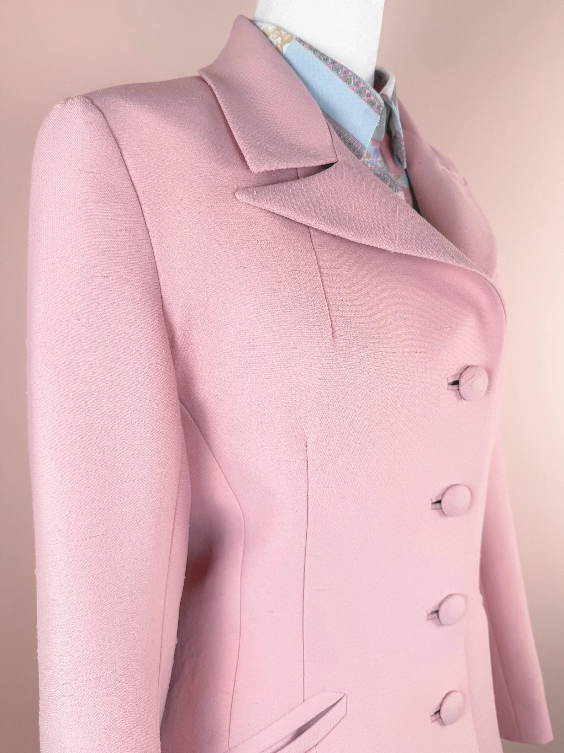 Light pink tailored blazer with a double-breasted design and rounded collar displayed on a mannequin against a soft pink background.