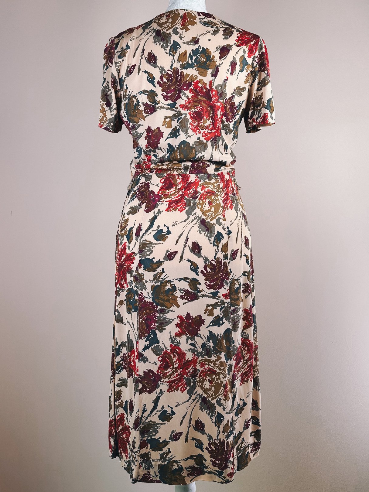 A vintage 1960s women's dress featuring a floral pattern with red, green, and gold flowers on a cream background, with short sleeves and a knee-length silhouette.