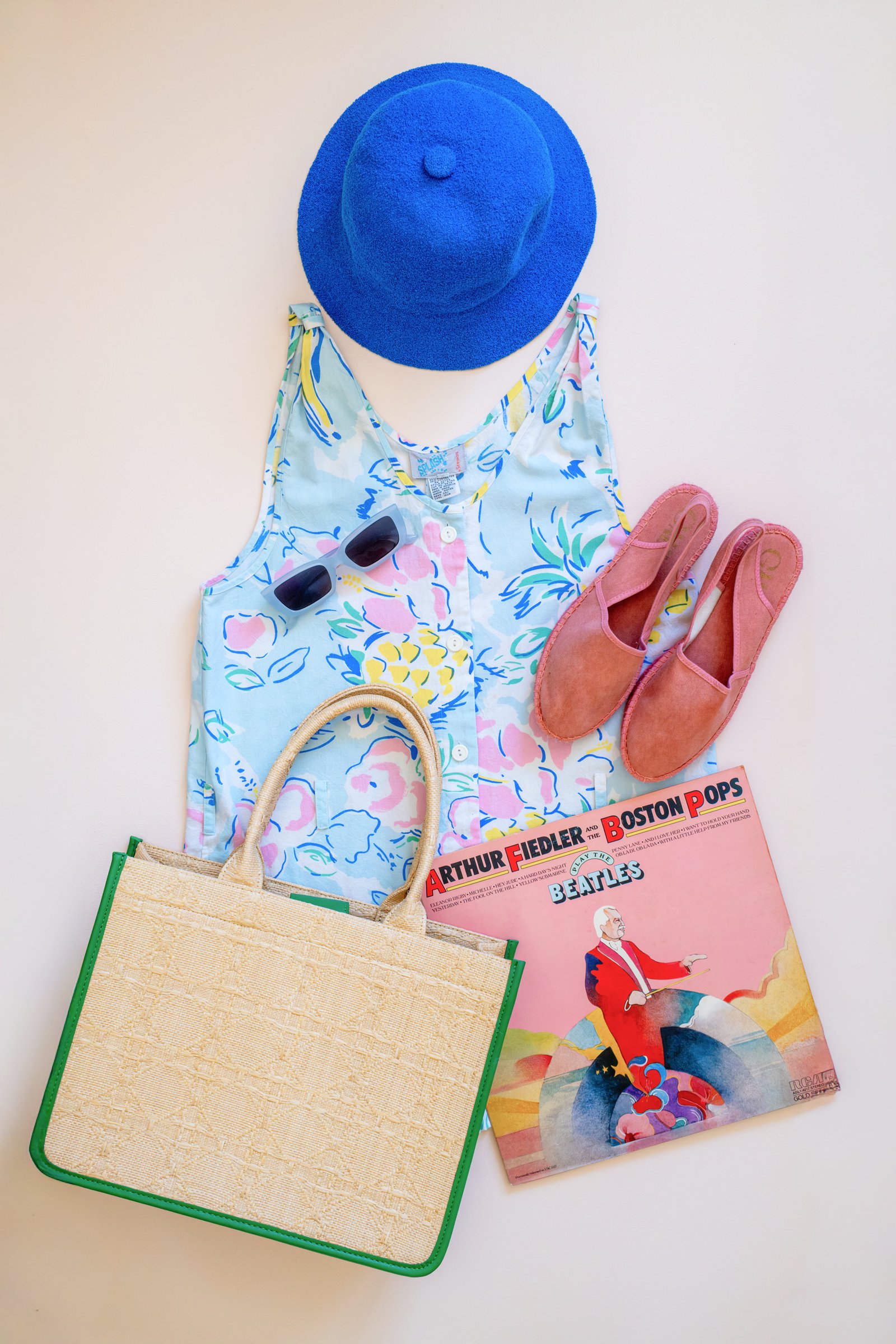Inspired by Summer, Styled by Music gallery image: A colorful floral dress, blue hat, sunglasses, pink sandals, a textured beige bag, and a vinyl record titled "Arthur Fiedler - Boston Pops" arranged together.