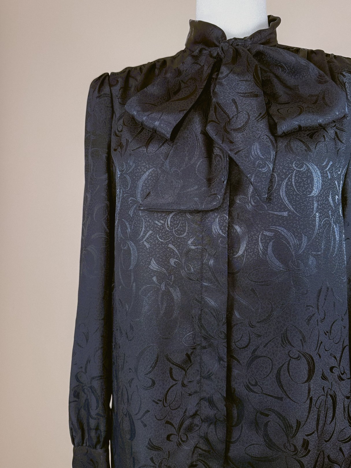 Black 1980s women's bow top in black with intricate patterned fabric and a high neck.