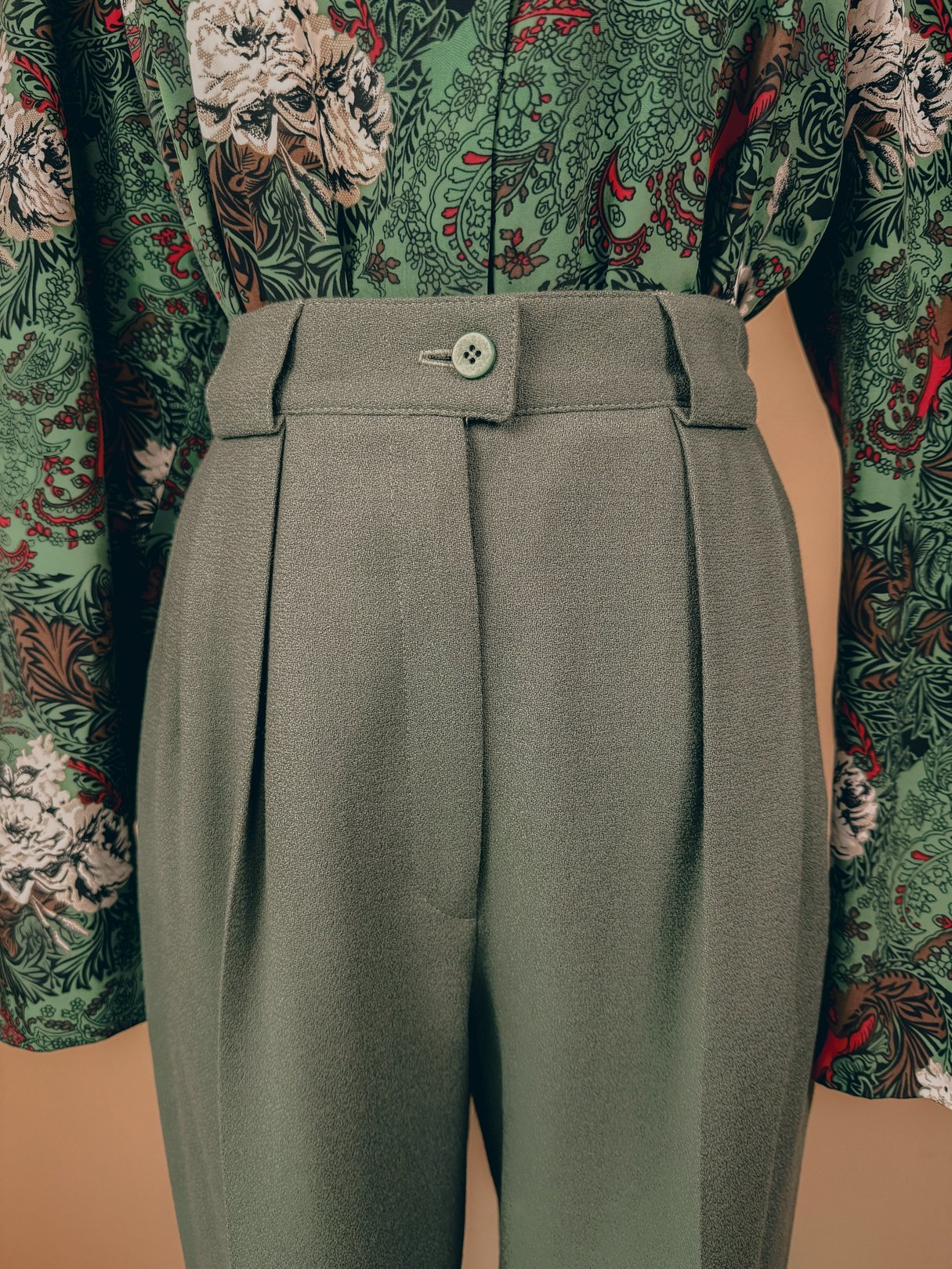 Sage green pleated trousers for women, featuring a high waist and tailored fit, styled in a 1980s fashion.