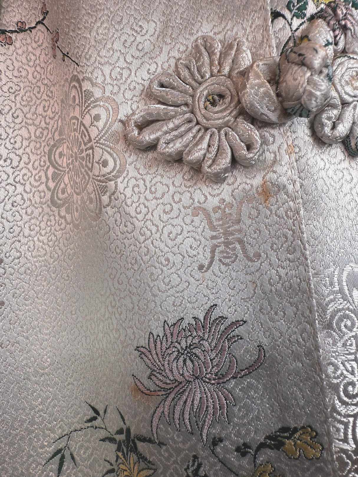 A silver silk cheongsam coat featuring intricate floral embroidery and decorative knots, reflecting 1970s style for women.