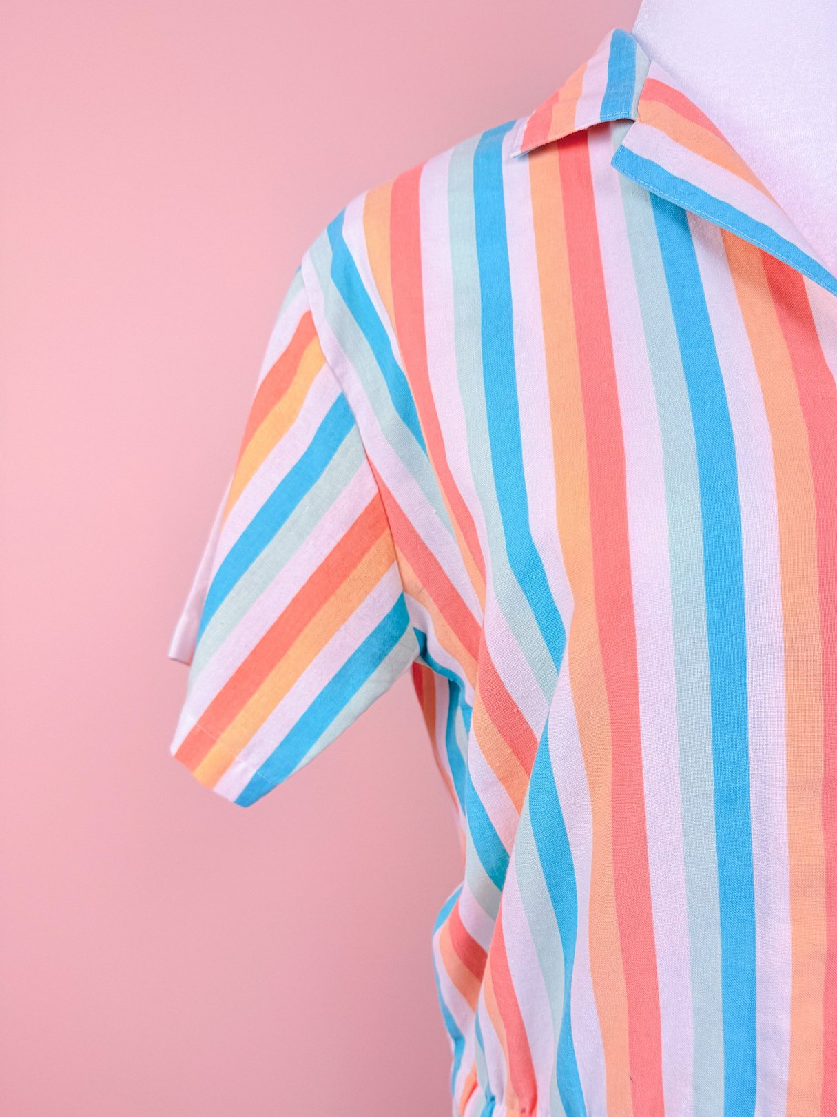 A blue, pink, and orange striped romper with short sleeves and a collar, suitable for women, reflecting an 1980s style.