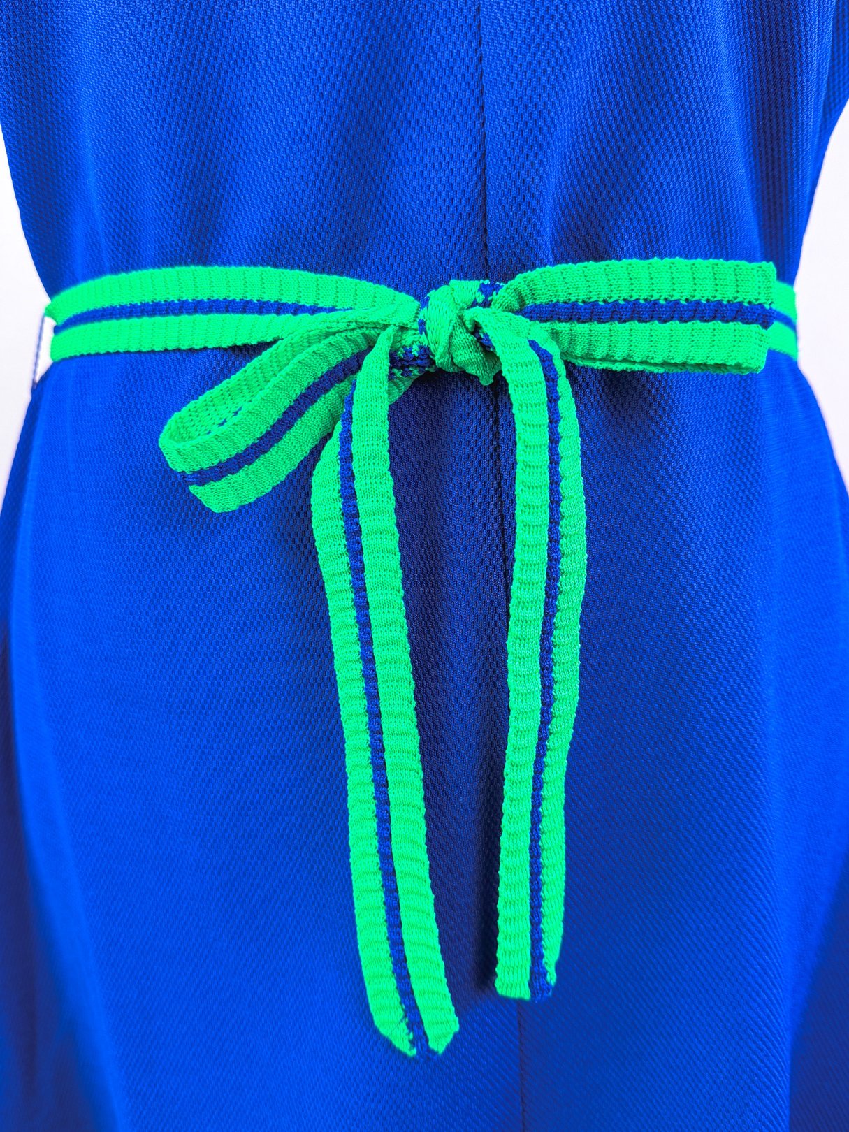 A blue 1970s women's dress features a green and blue striped belt tied at the waist.