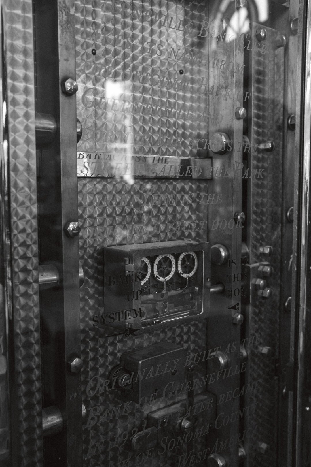 A vintage bank vault door featuring intricate textured metalwork and engraved text.