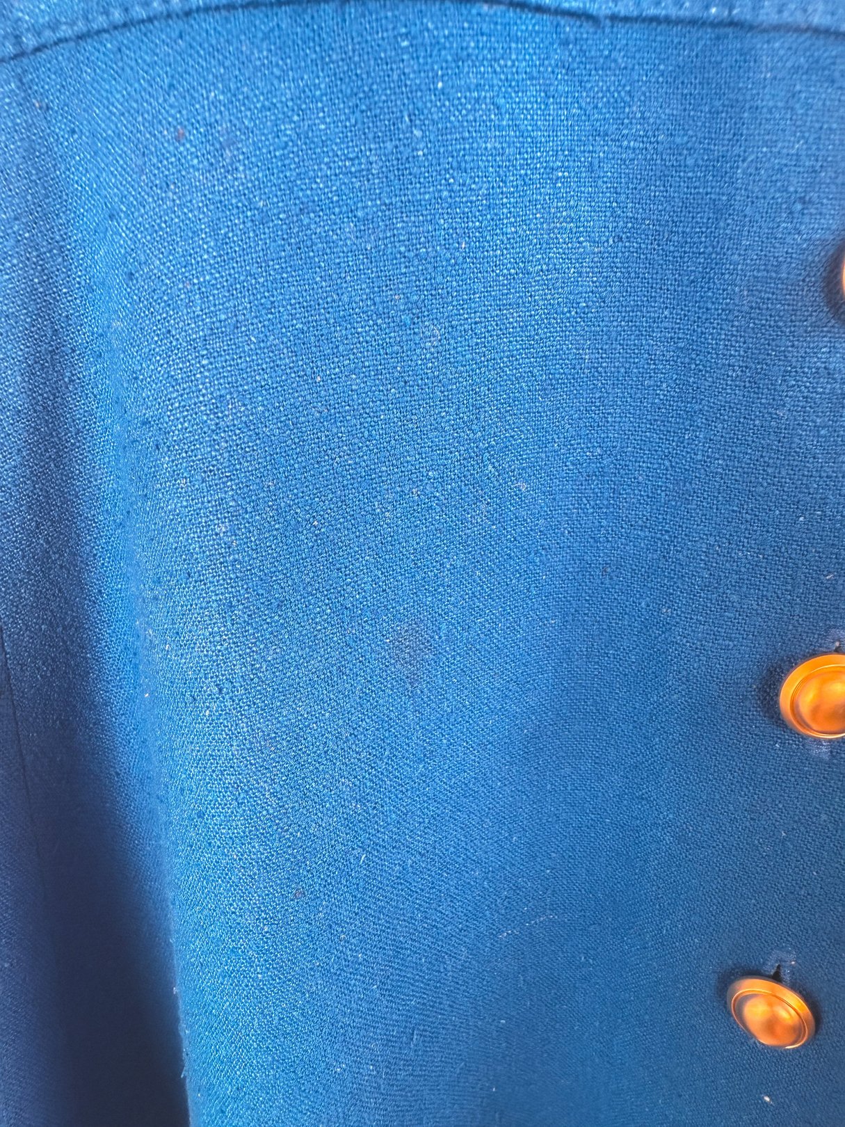 Cerulean blue fabric of a women's 1980s dress featuring decorative orange buttons.