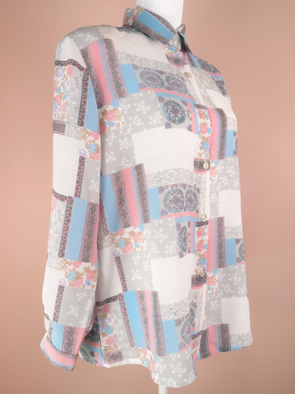 White patchwork blouse featuring floral and geometric patterns, long sleeves, and a collared neckline, typical of the 1980s women's fashion.
