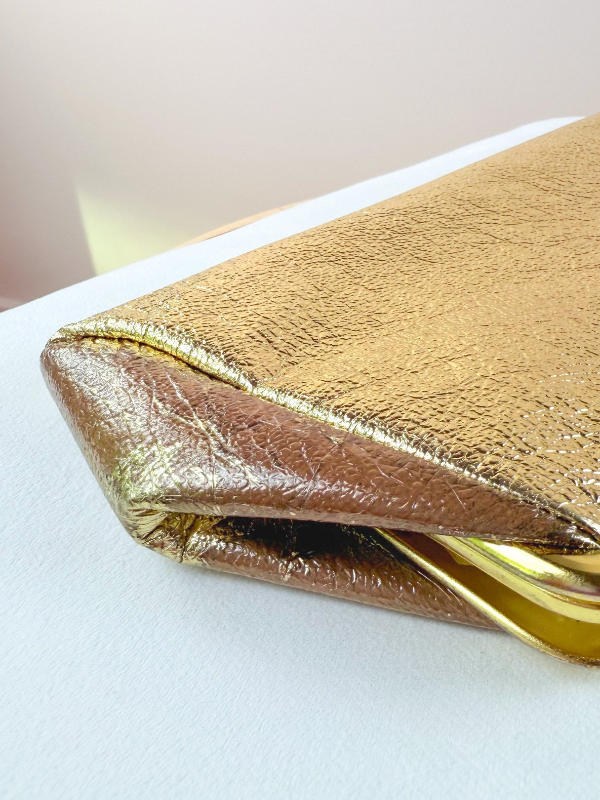 A gold 1950s-style clutch bag with a textured metallic finish, featuring a sleek, angular design.