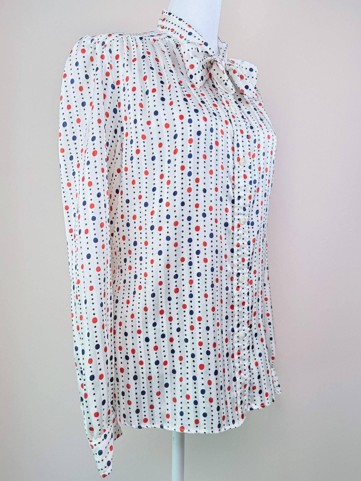 Women’s 1980s blouse featuring a white fabric with red and blue polka dots, a collared neckline, and long sleeves.