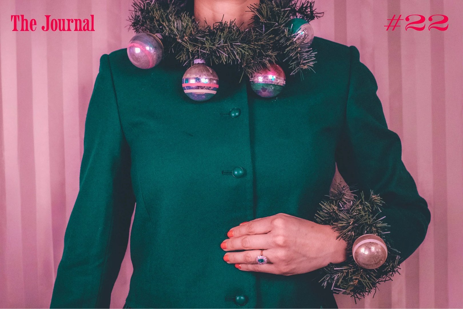 A person wearing a green jacket adorned with a festive garland and colorful ornaments around the neck and wrist.