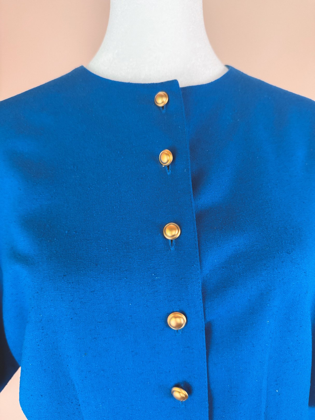 Cerulean blue dress with a high neckline and gold buttons down the front, designed for women and inspired by the 1980s era.