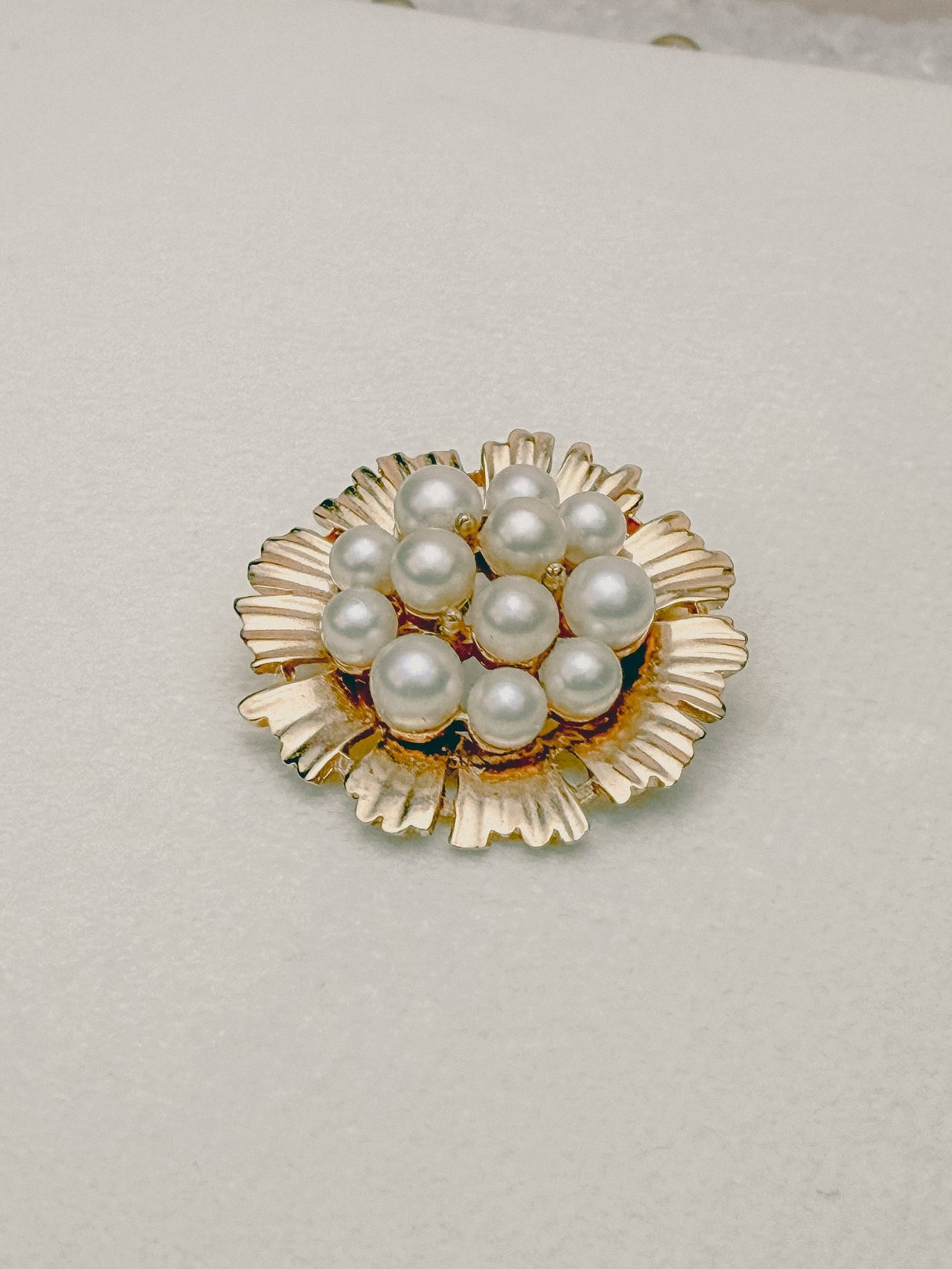 Gold-tone brooch featuring a floral design adorned with several white pearls, reflecting 1970s costume jewelry style for women.